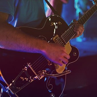 Musician playing a semi-hollow guitar on stage, showcasing live performance skills at TheBandBuilder.com