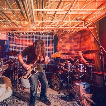 Musicians playing guitar and drums in a cozy studio, capturing the essence of band practice at TheBandBuilder.com